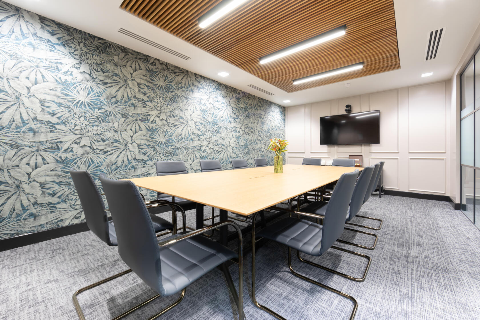A meeting centre with a large conference table, blue chairs, patterned accent wall, and wall-mounted screen at Landmark: Farringdon, London.