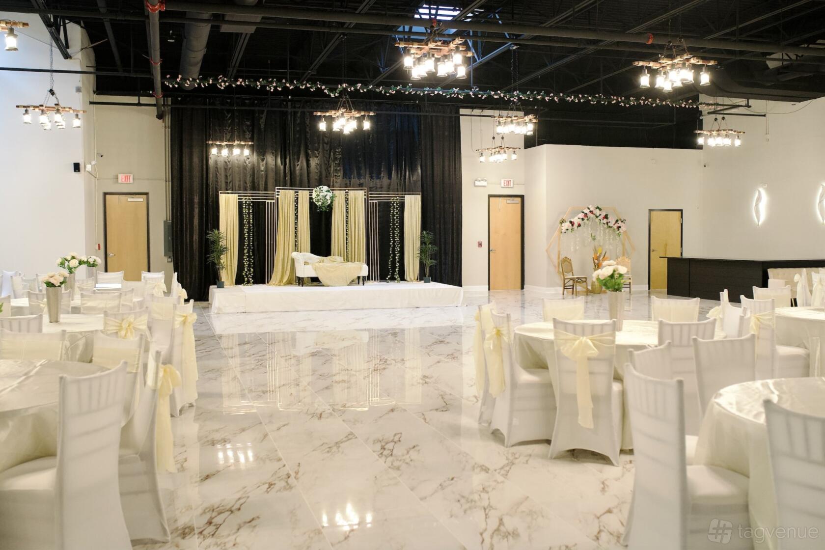 An event venue with marble floors, round tables with white chairs, and a decorated stage at Red Rose Banquets.