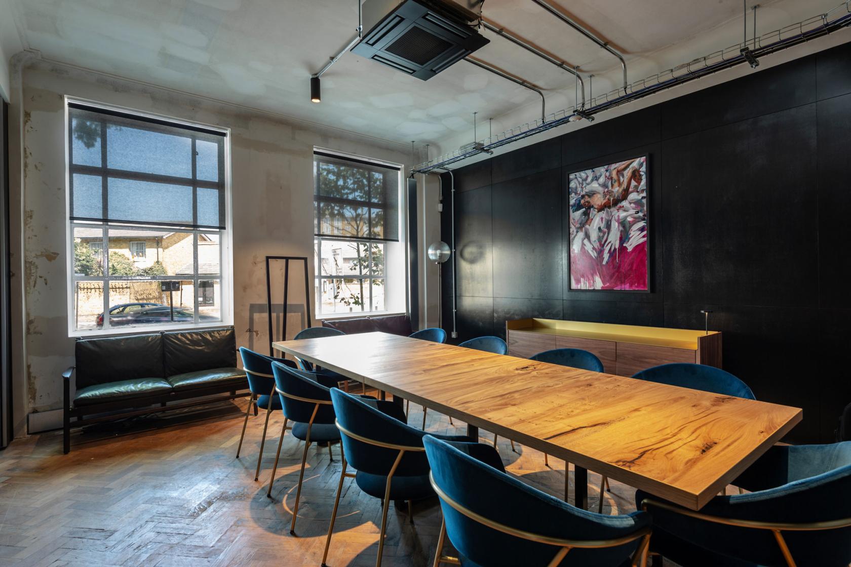 A meeting room with a long wooden table, blue velvet chairs, large windows, and wall art at The Ministry.