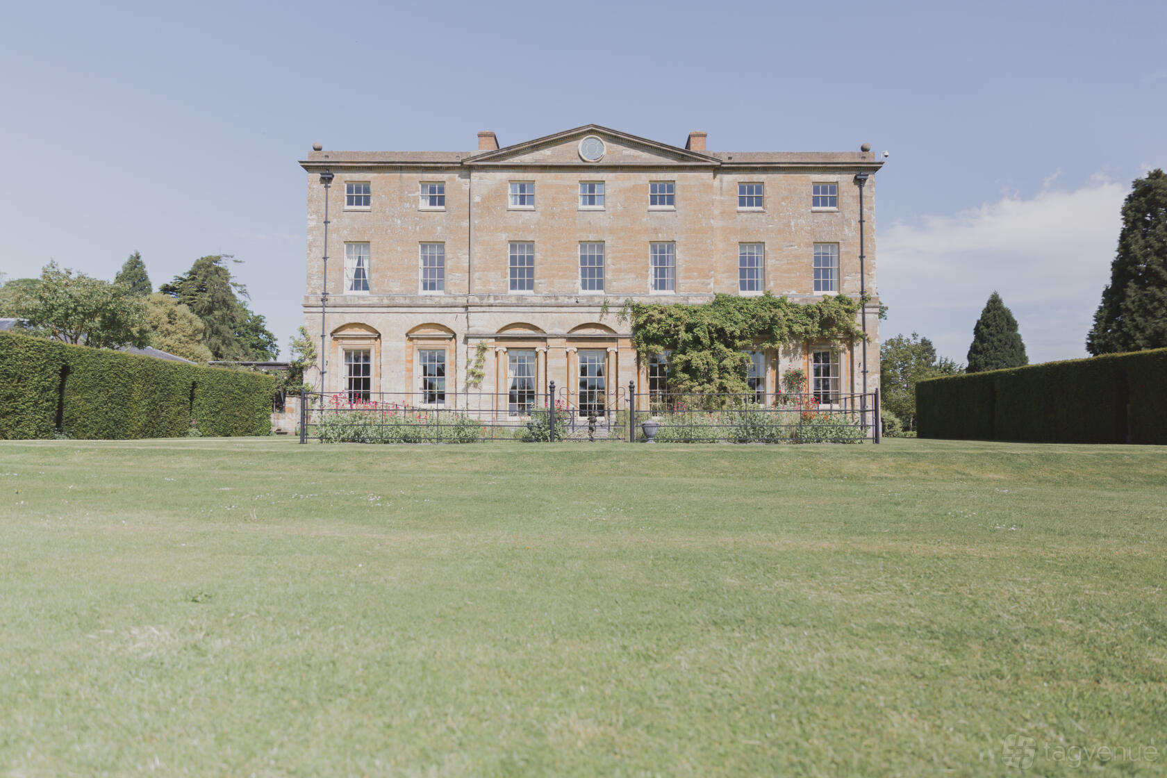 A country house with a symmetrical stone facade, tall windows, and manicured lawns at Courteenhall Estate.
