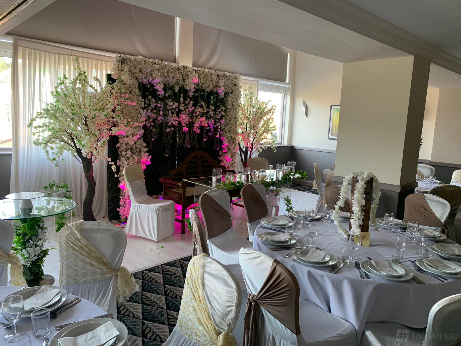 An event space with round tables, white and gold chairs, and a floral stage backdrop at Holiday Inn Leicester - Wigston.