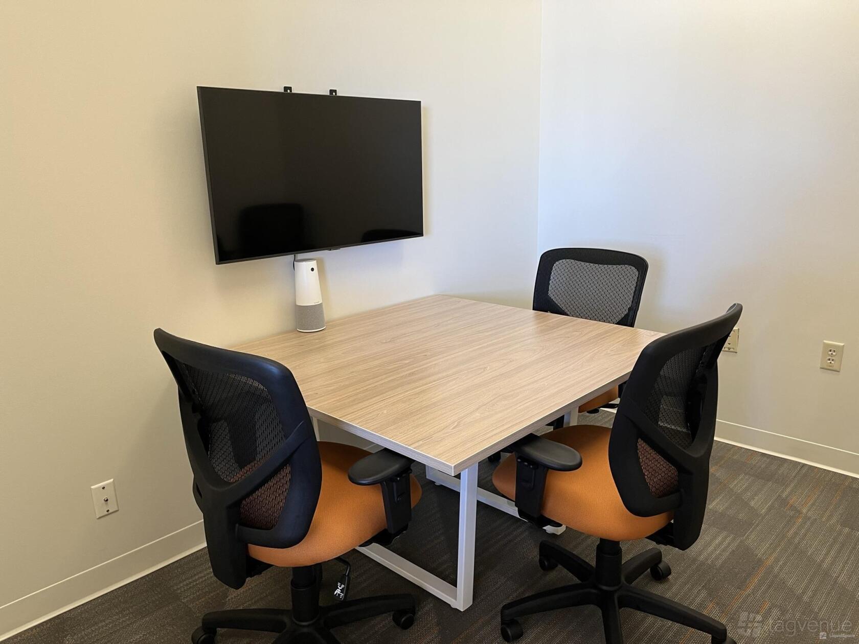 A meeting room with a wall-mounted screen, four mesh chairs, and a square wooden table at Office Evolution San Antonio.