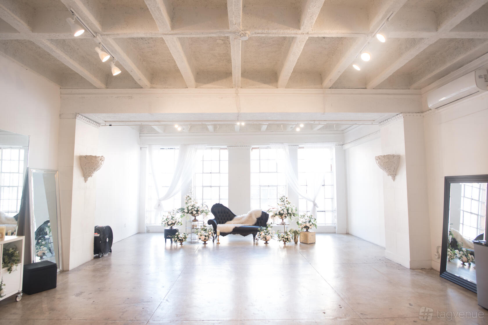 An event venue with tall grid windows, white walls, exposed concrete ceiling, and lounge seating at Skyline GRAND.