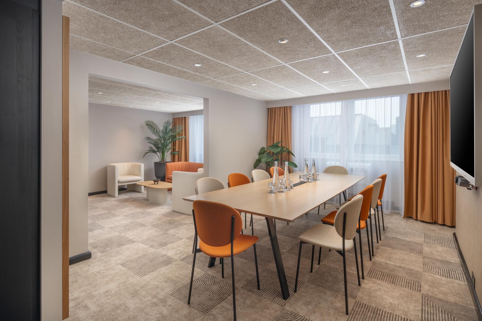 A meeting room with a long wooden table, cushioned chairs, natural light, and a lounge area at Mercure London Earl's Court.
