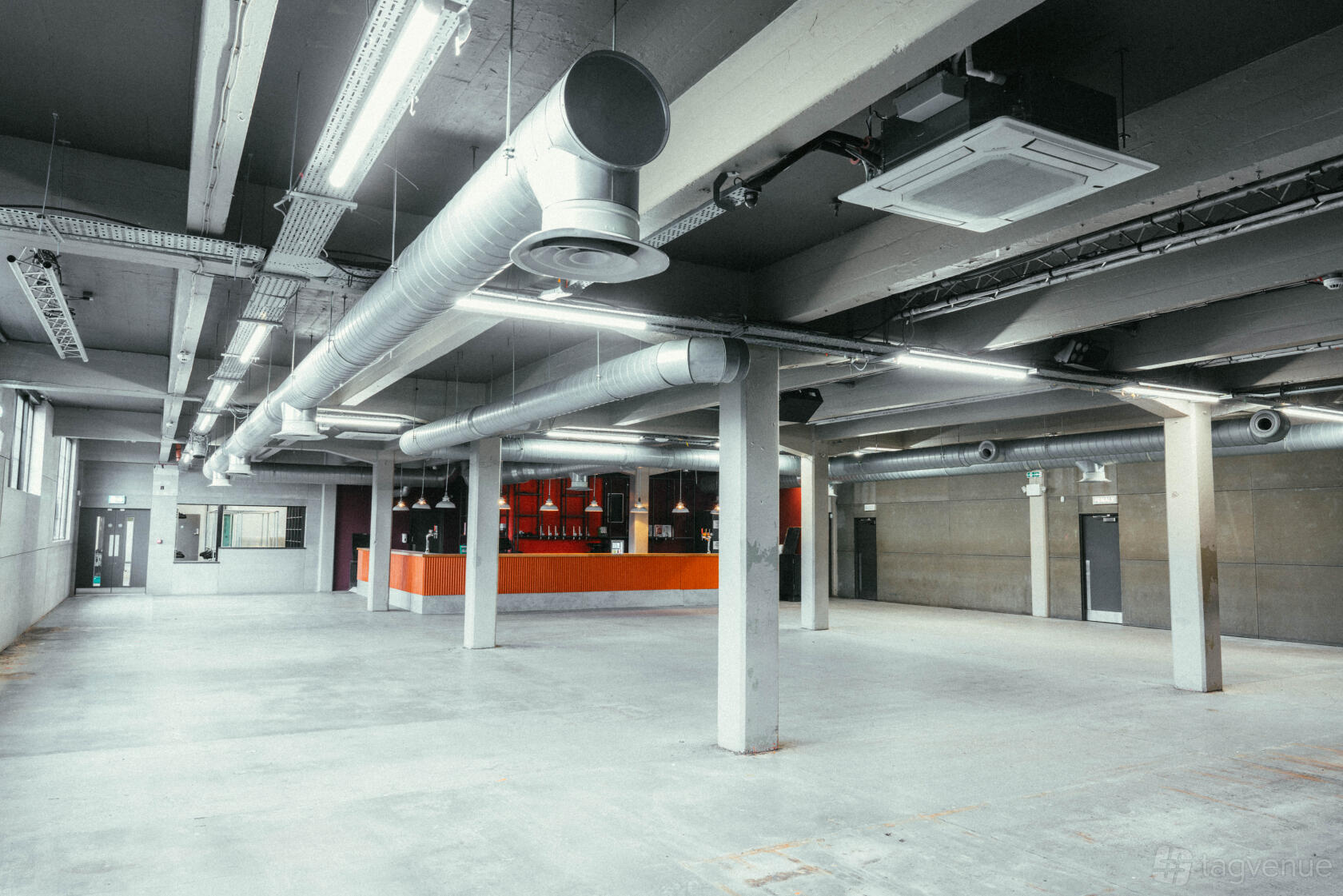 An industrial event venue with exposed ductwork, concrete floors, and a long orange bar at SWG3.