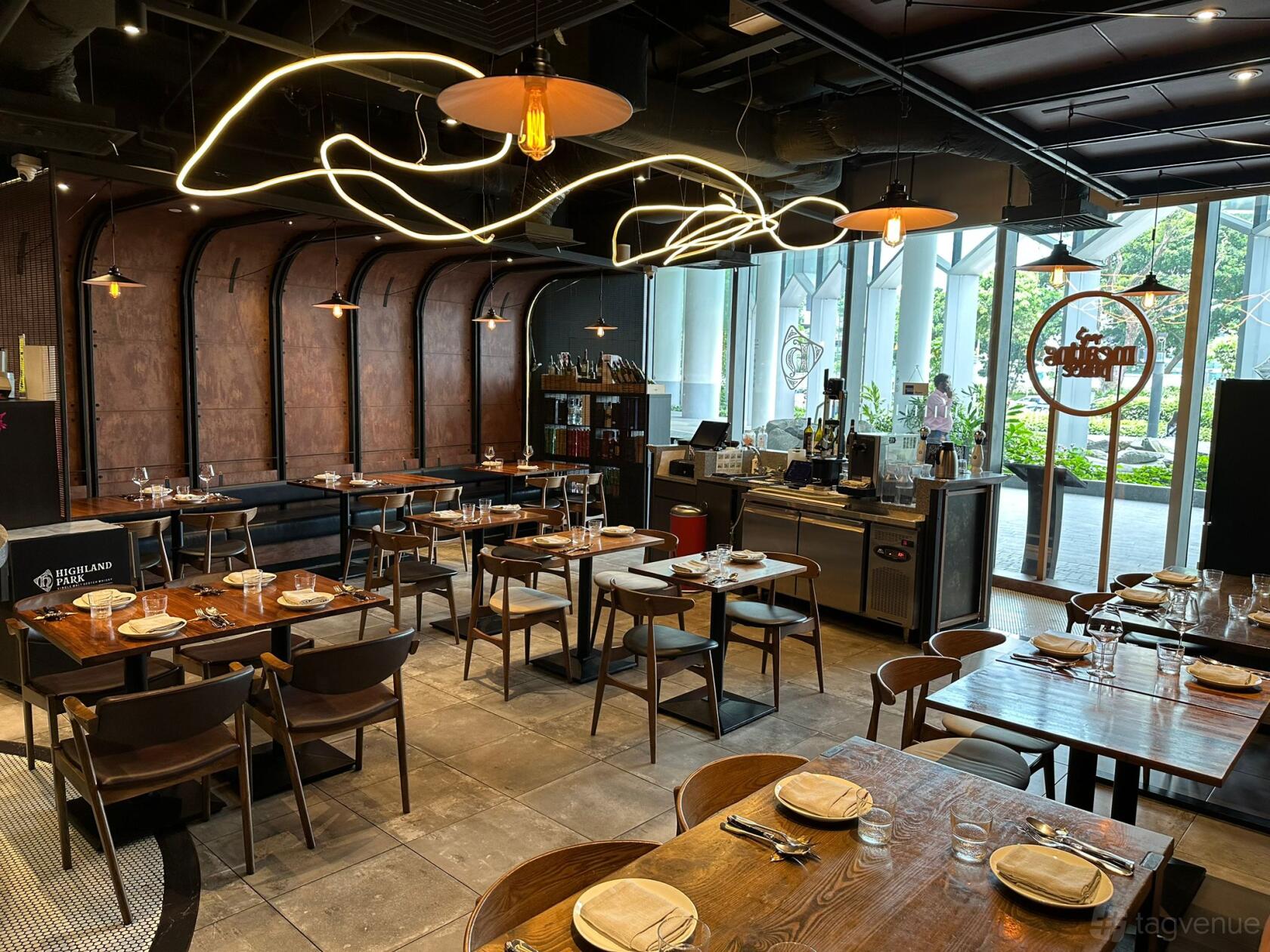 A restaurant with floor-to-ceiling windows, decorative lighting, and wooden tables set for dining at Meating Place.