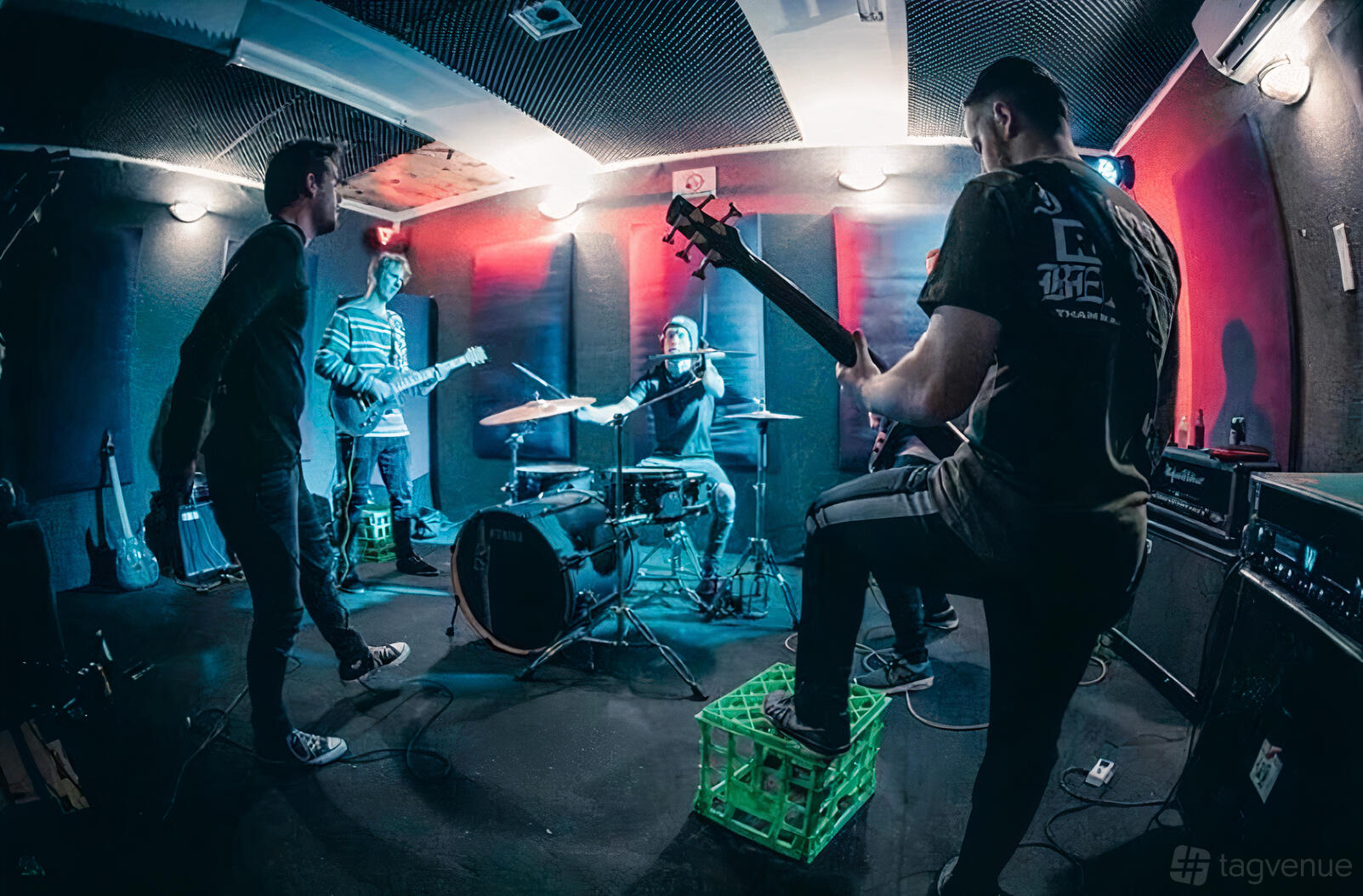A rehearsal room with acoustic wall panels, drum kit, electric guitars, and colored stage lighting at Bayside Rehearsal Studios.
