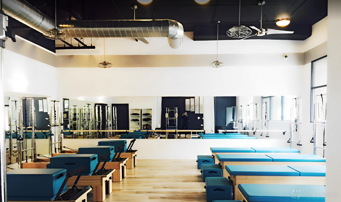 A dance studio with mirrored walls, light wood floors, and blue Pilates reformer machines at Pilates of San Diego - Downtown Location.
