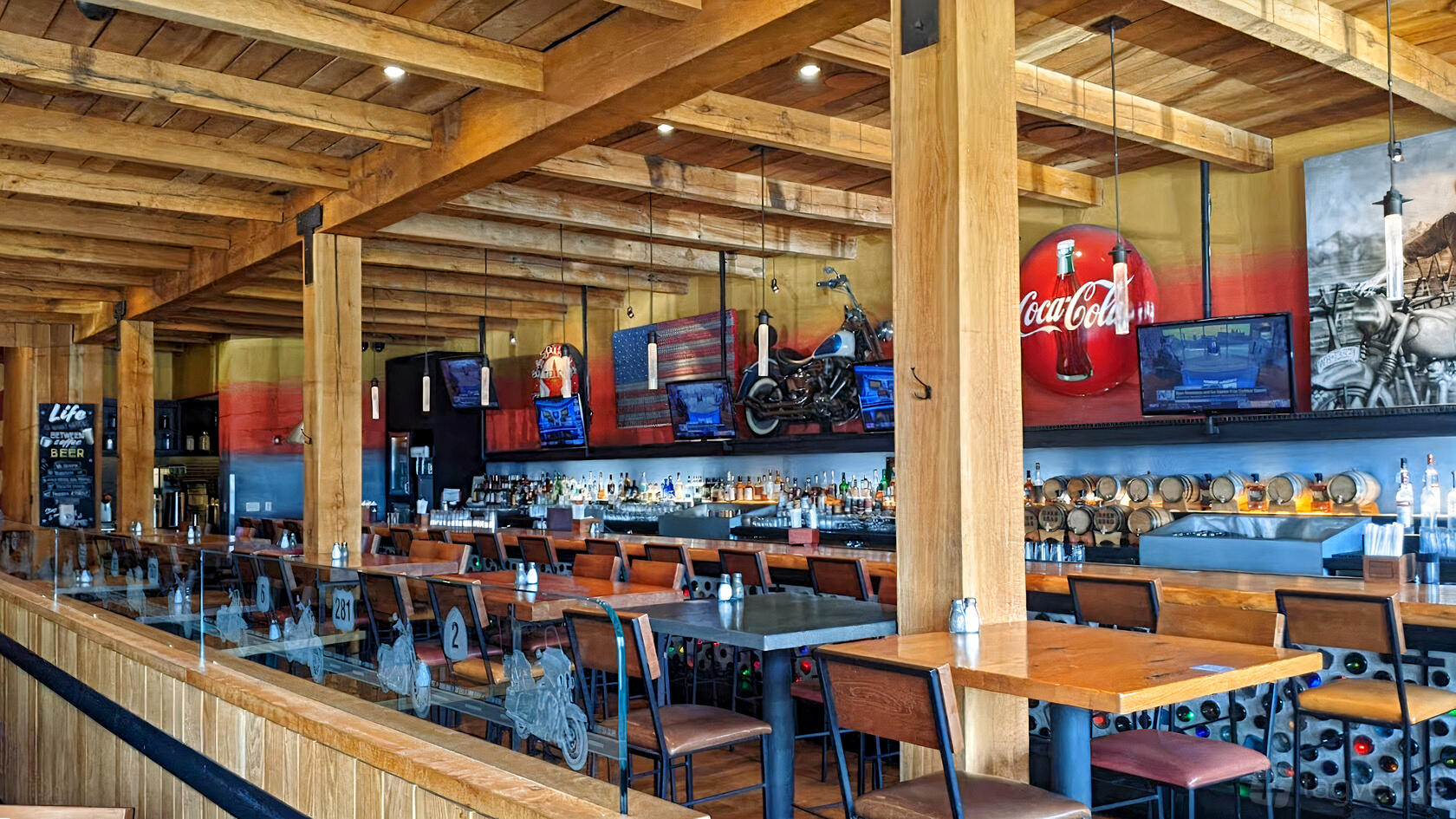 An event space in a bar with wood beam ceilings, mounted TVs, and high-top tables at Open Road - Merrifield.