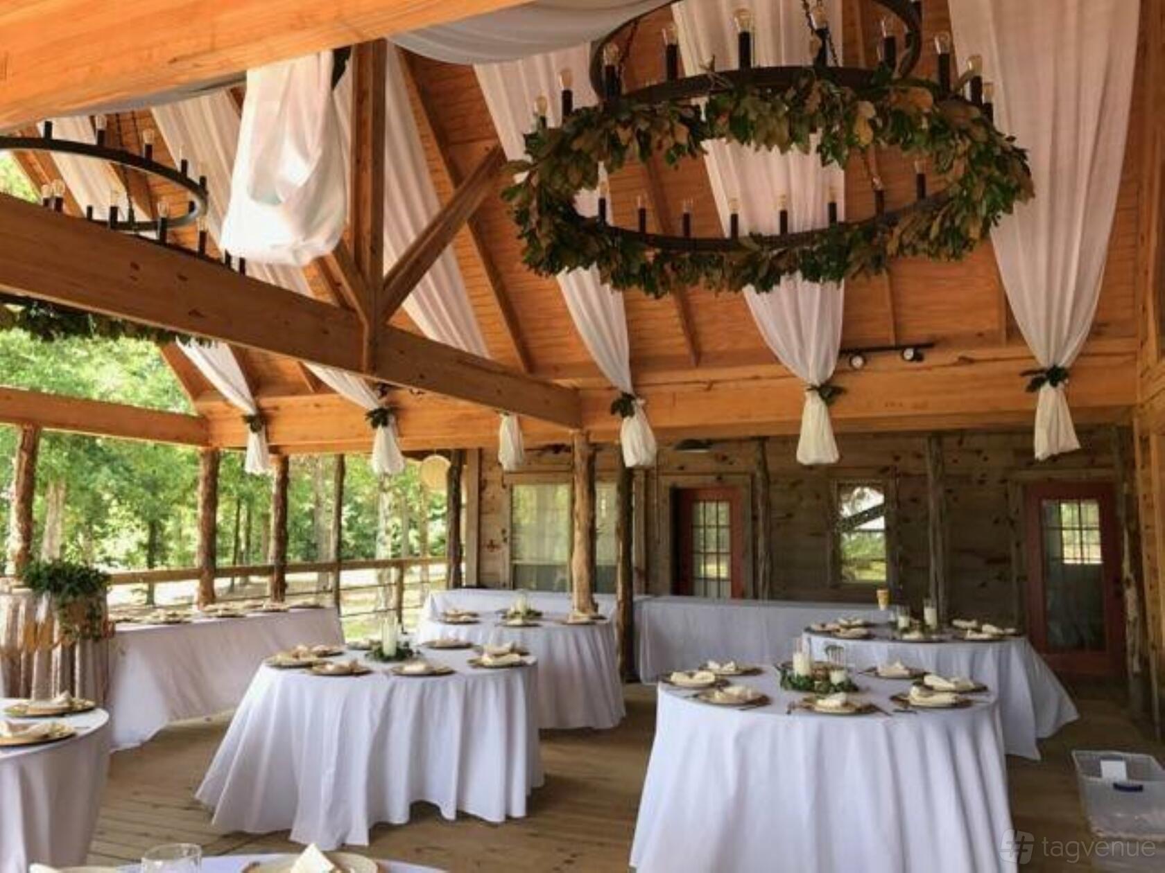 An indoor event venue with exposed wooden beams, draped white fabric, and round tables with white linens at Wylde Acres.