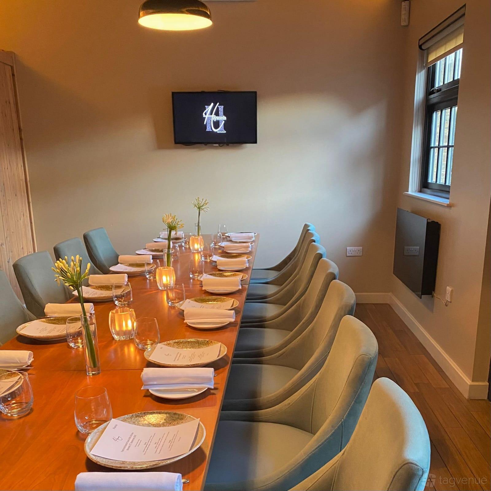 A dining room with a long wooden table, blue upholstered chairs, candlelight, and floral centerpieces at Haywards.