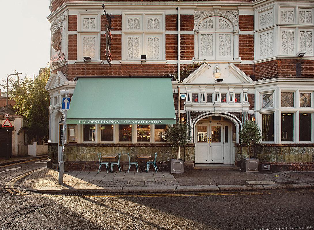 A bar with ornate brickwork, large windows, and outdoor seating at Paradise By Way of Kensal Green.