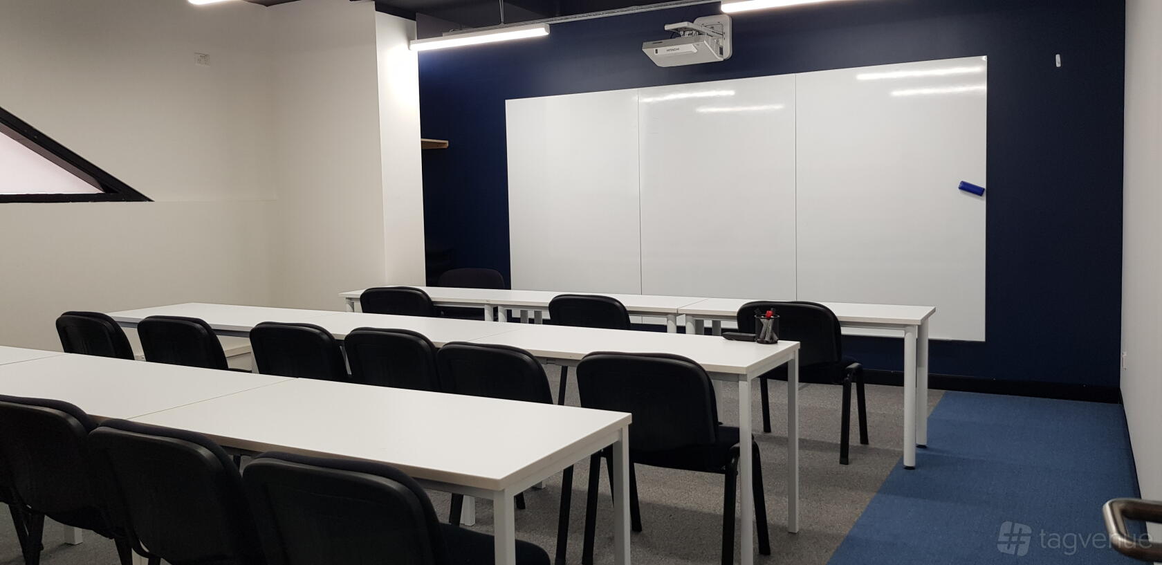 A classroom with white tables, black chairs, a large whiteboard, and a ceiling projector at Burwood Learning Centre.