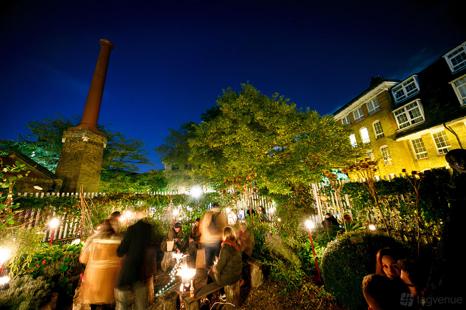 An outdoor museum garden with lush greenery, trees, string lights, and guests at The Brunel Museum.