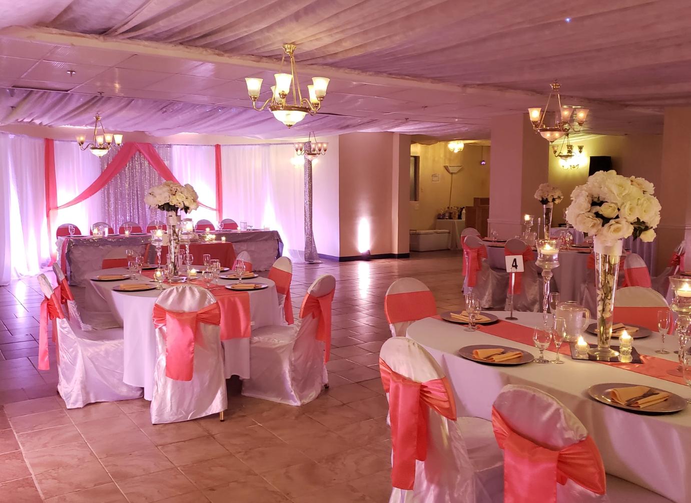 A banquet hall with draped fabric, chandelier lighting, and round tables with white linens and pink accents at Occasions Banquet & Catering Hall.