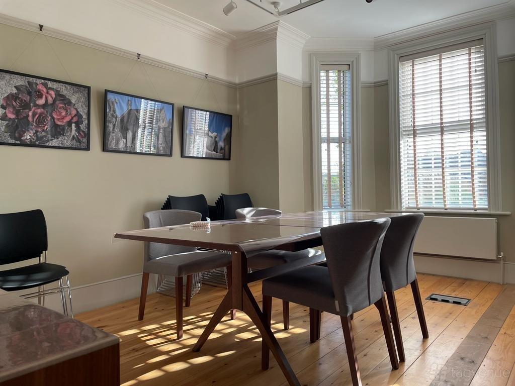 A meeting room with a wooden table, upholstered chairs, large windows with blinds, and framed art at House of Life Heritage Centre.