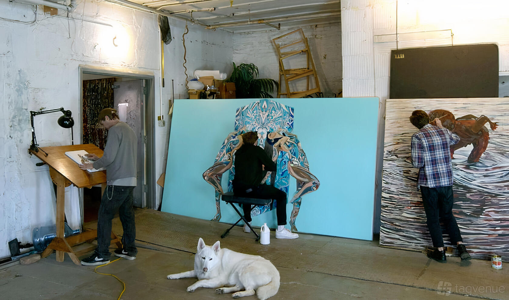 A gallery studio with artists working on large canvases, exposed pipes, and a white brick wall at The Greenpoint Gallery.