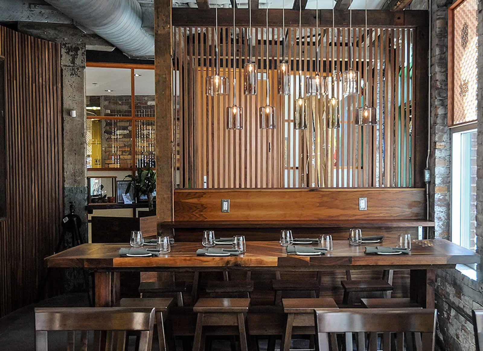 An event space in a restaurant with a long wooden table, pendant lights, and slatted wood dividers at BOKU Japanese Eats + Drinks.