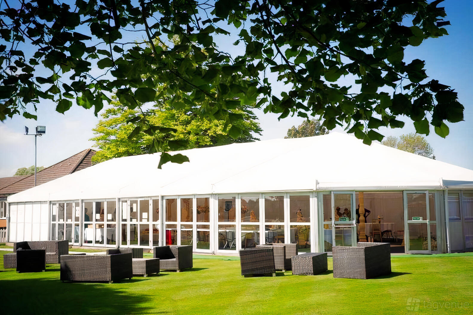A hall with a large white marquee, floor-to-ceiling windows, and outdoor wicker seating on the lawn at Leicester Racecourse.