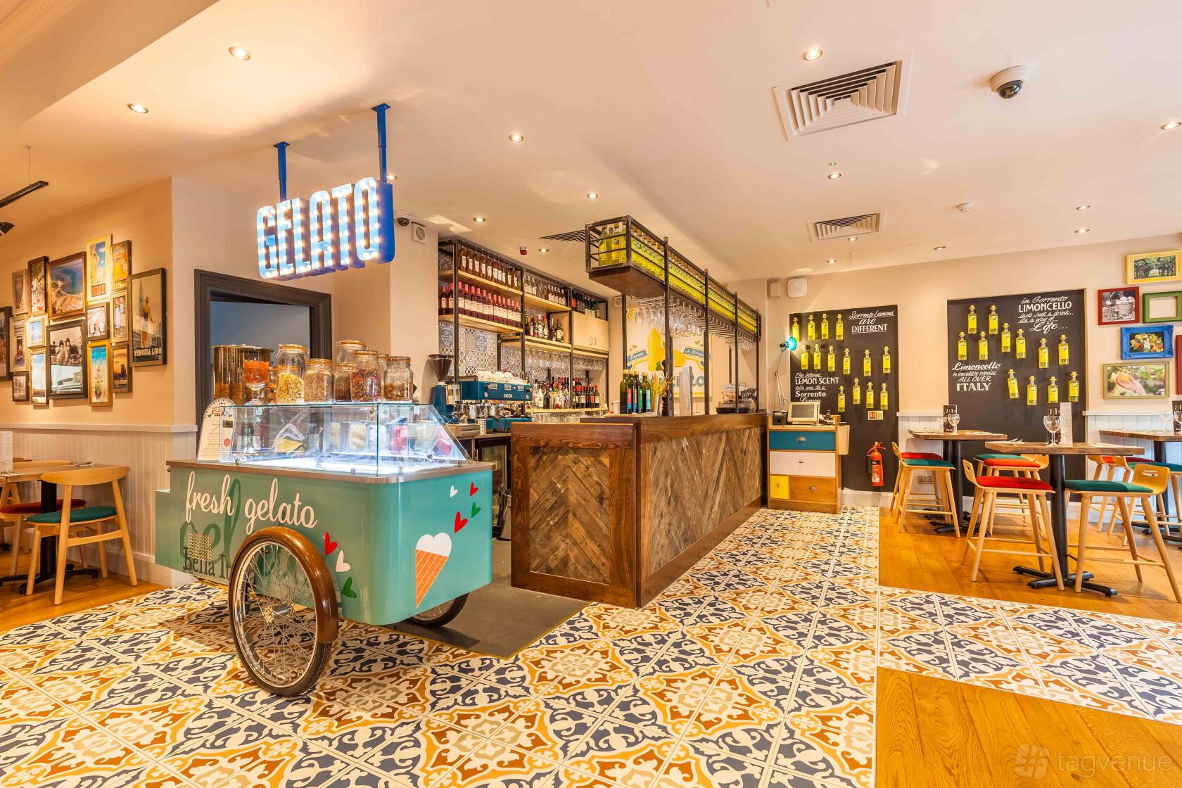 A restaurant with patterned tile flooring, a wood bar, colorful chairs, wall art, and a gelato cart at Bella Italia - Nottingham Cornerhouse.