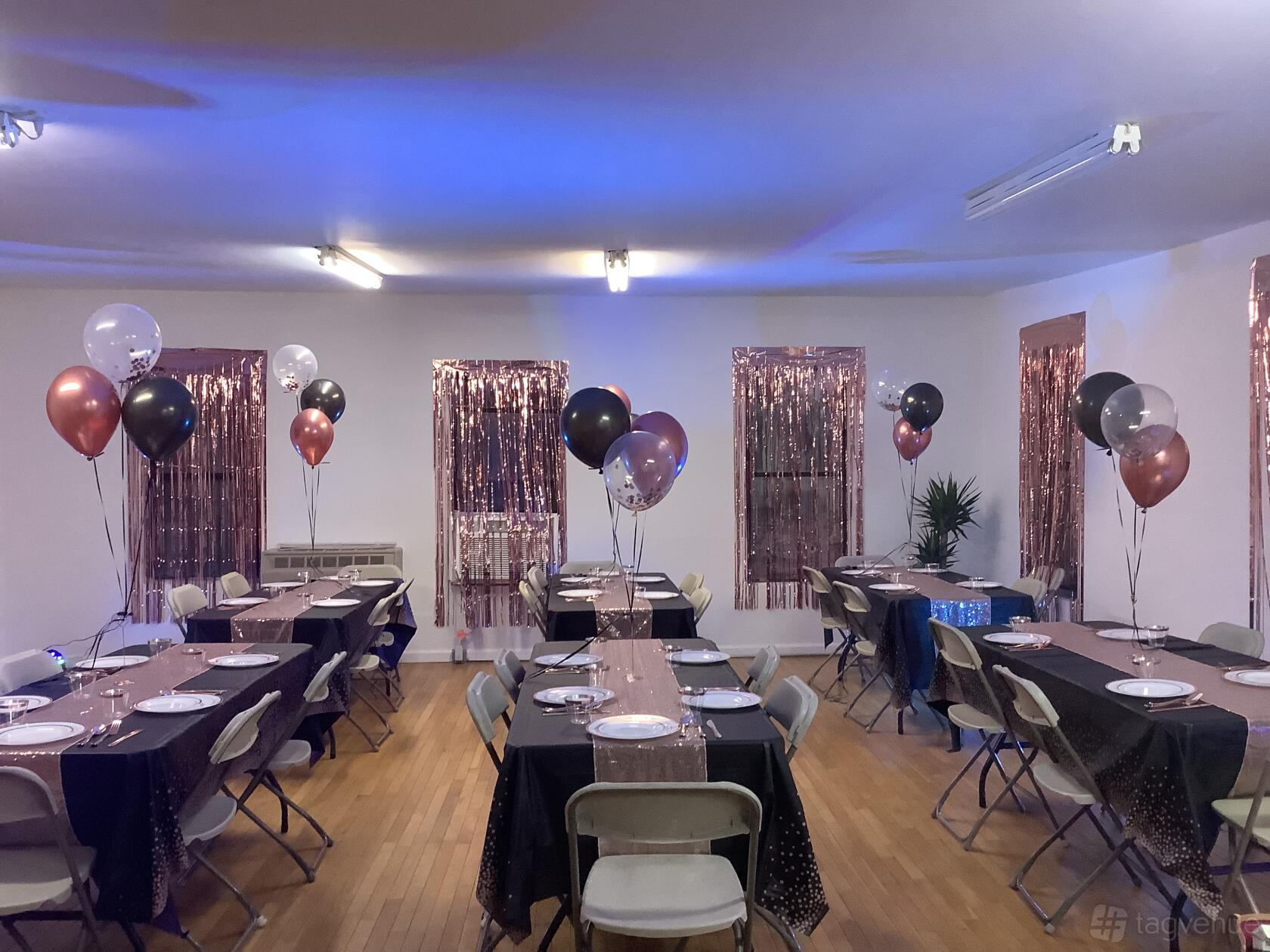 An event venue with decorated tables, metallic streamers on windows, and balloon centerpieces at The Party Room NYC.