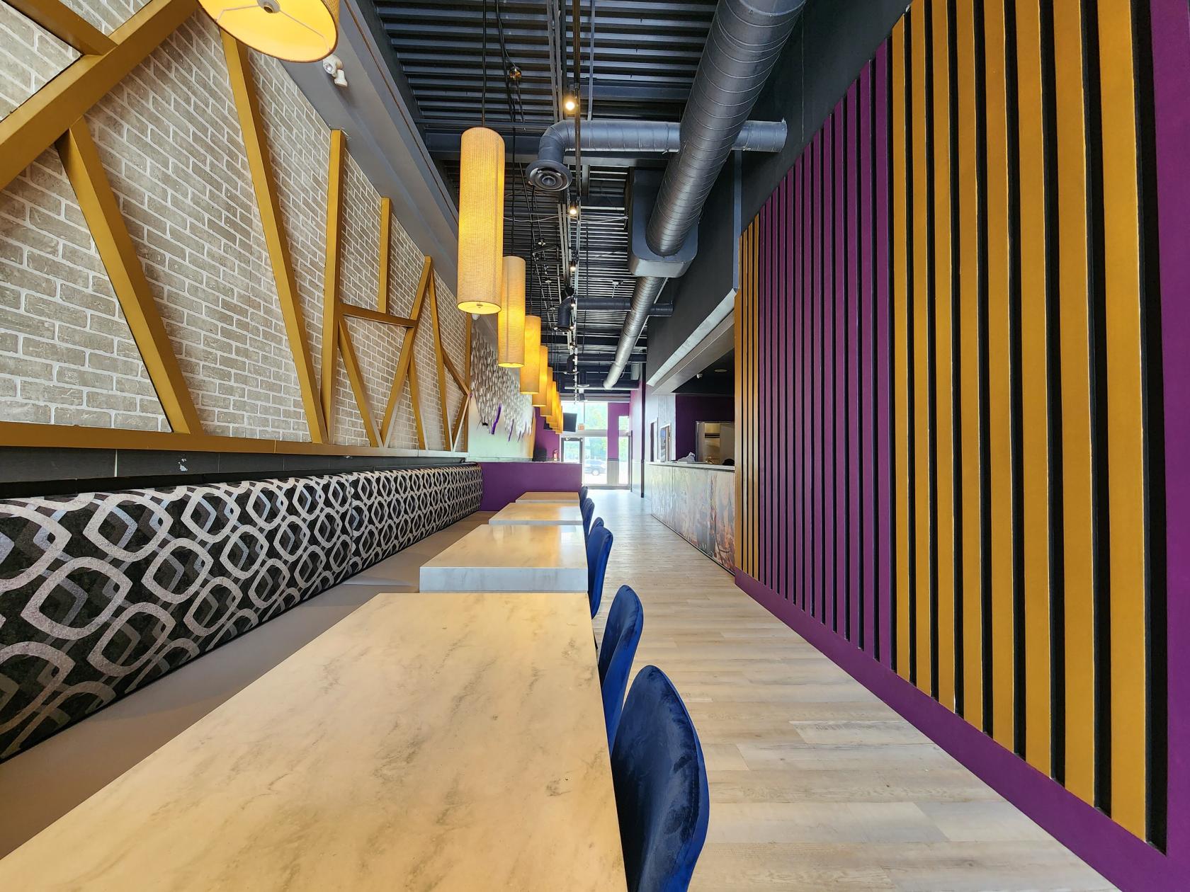 A bar with marble tables, patterned bench seating, and geometric wood wall accents at Gomoku Restaurant and Bar.