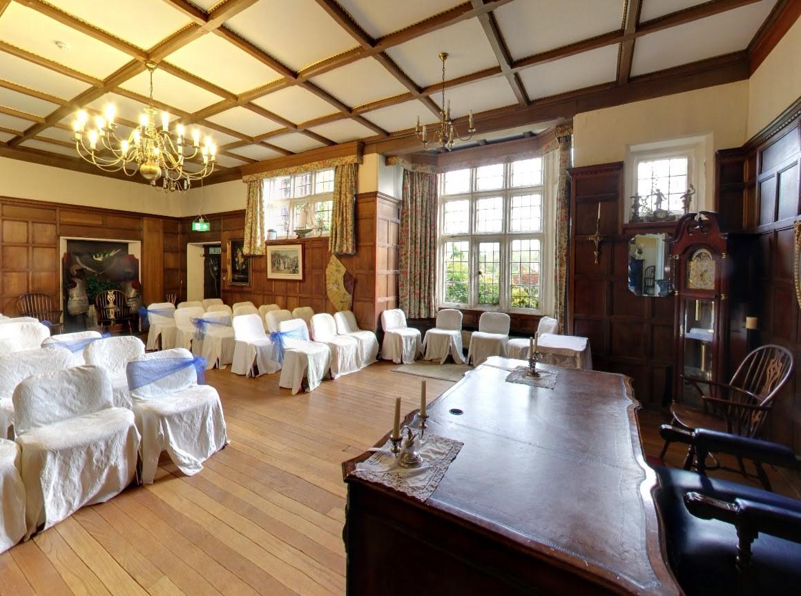 An event space with wood-paneled walls, leaded windows, and white chair covers arranged for a ceremony at Heskin Hall.