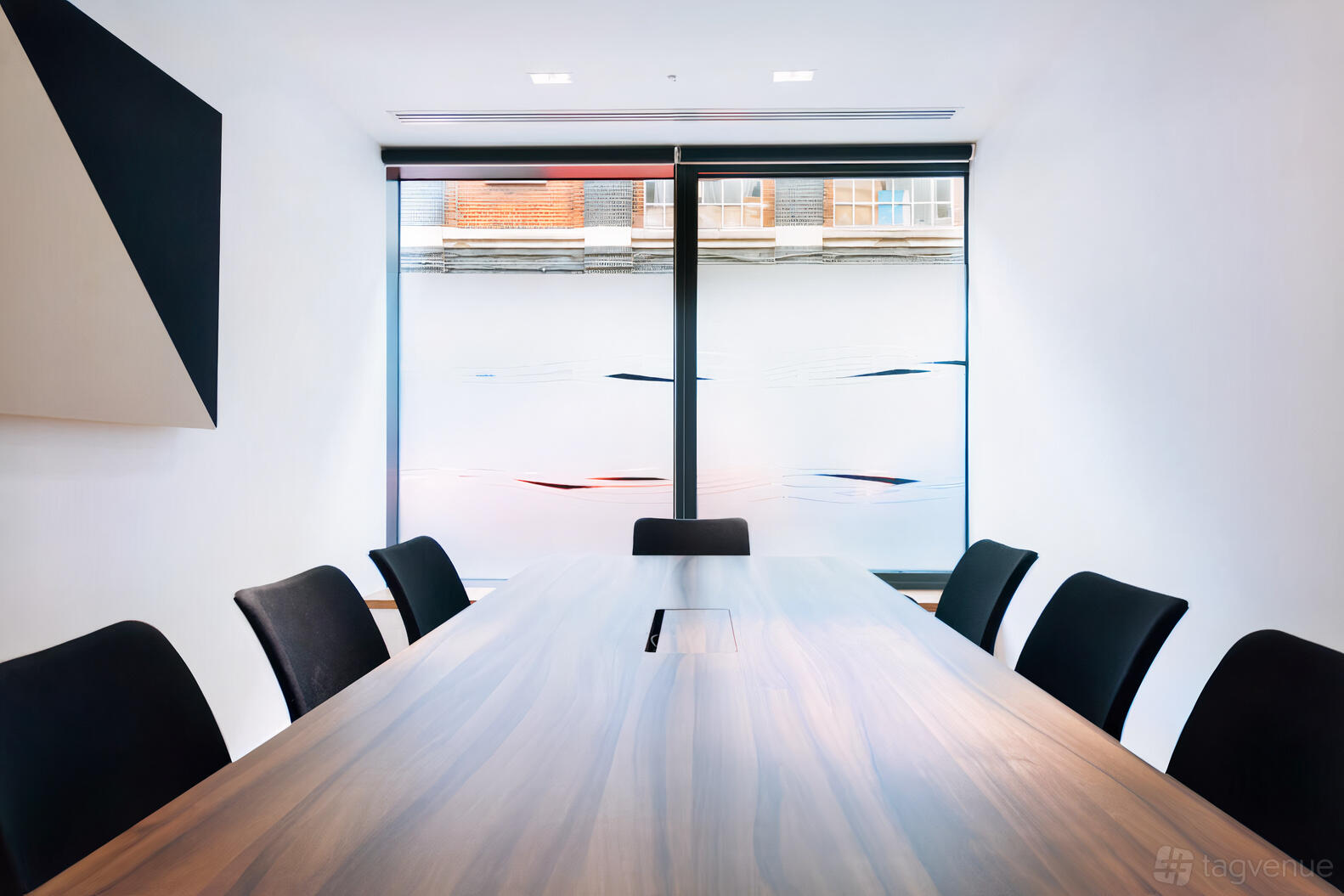 A conference centre boardroom with a long wooden table, black chairs, and large frosted windows at Us&Co Stratford.