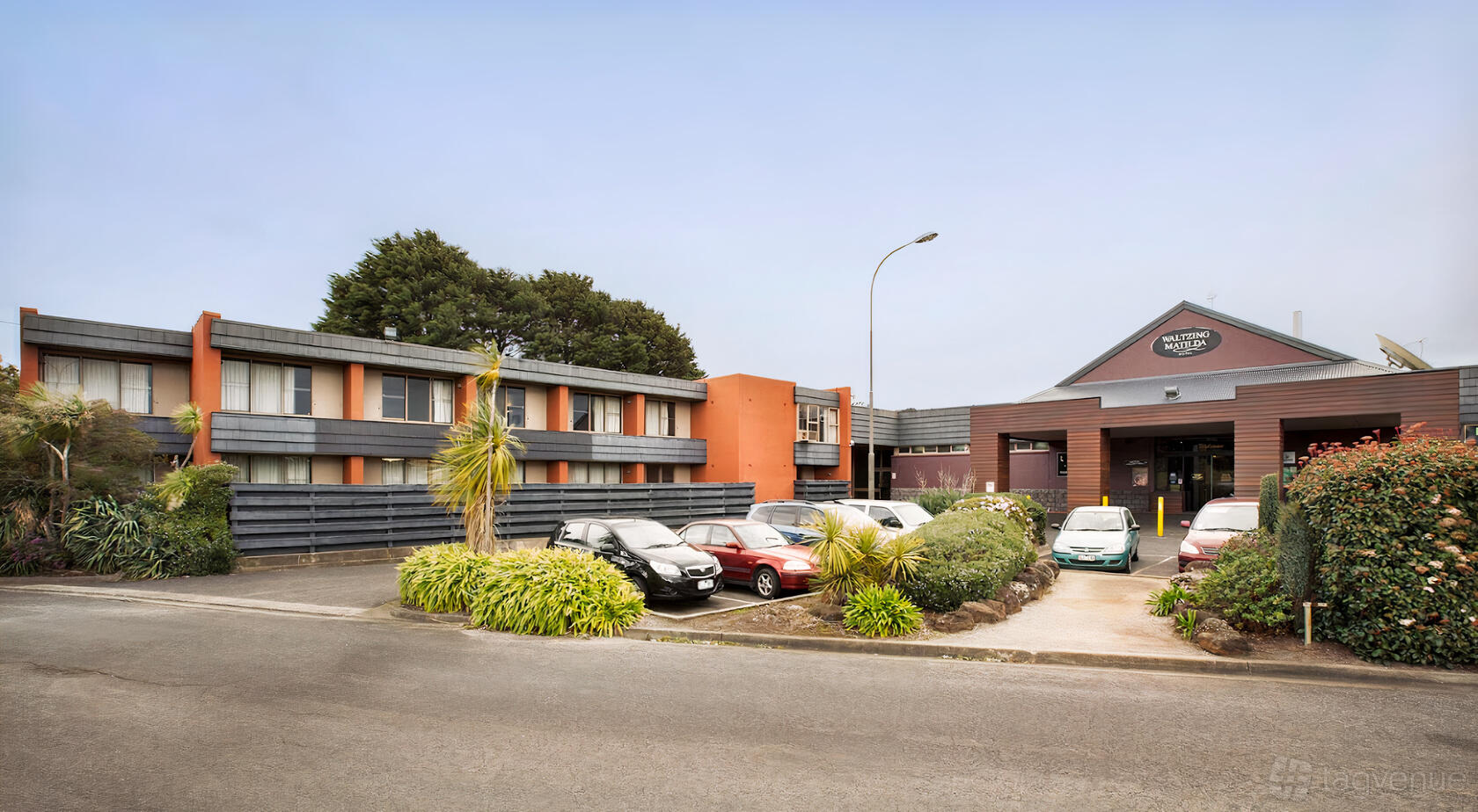 A hotel with a two-story exterior, landscaped greenery, and guest parking at Waltzing Matilda Hotel.
