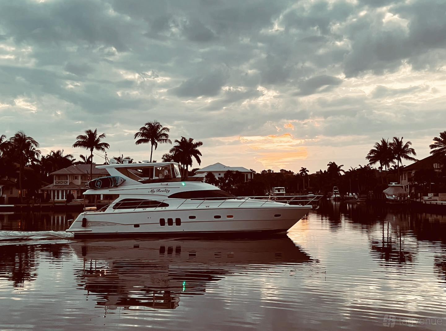 A white yacht with an upper deck cruising along calm water at sunset, surrounded by palm trees at Lots Of Yachts/Lots Of Spots South Florida.