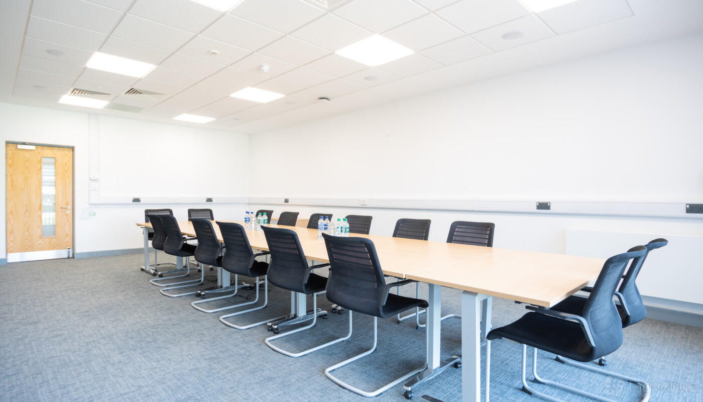 A conference centre room with a long rectangular table, black chairs, and water bottles at Rothamsted Conference Centre.