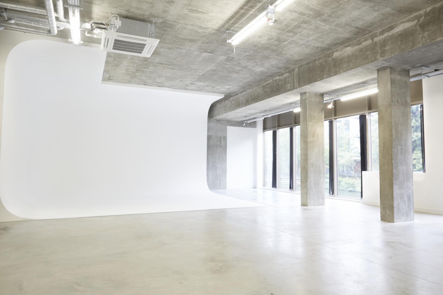 A blank canvas studio with a white cyclorama wall, concrete pillars, and floor-to-ceiling windows at LOCK Studios.