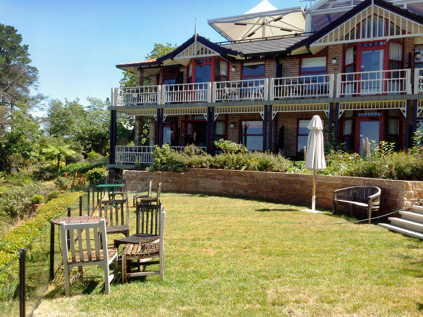 A hotel with a brick facade, wraparound balconies, and a grassy lawn with wooden tables at Echoes Boutique Hotel & Restaurant.