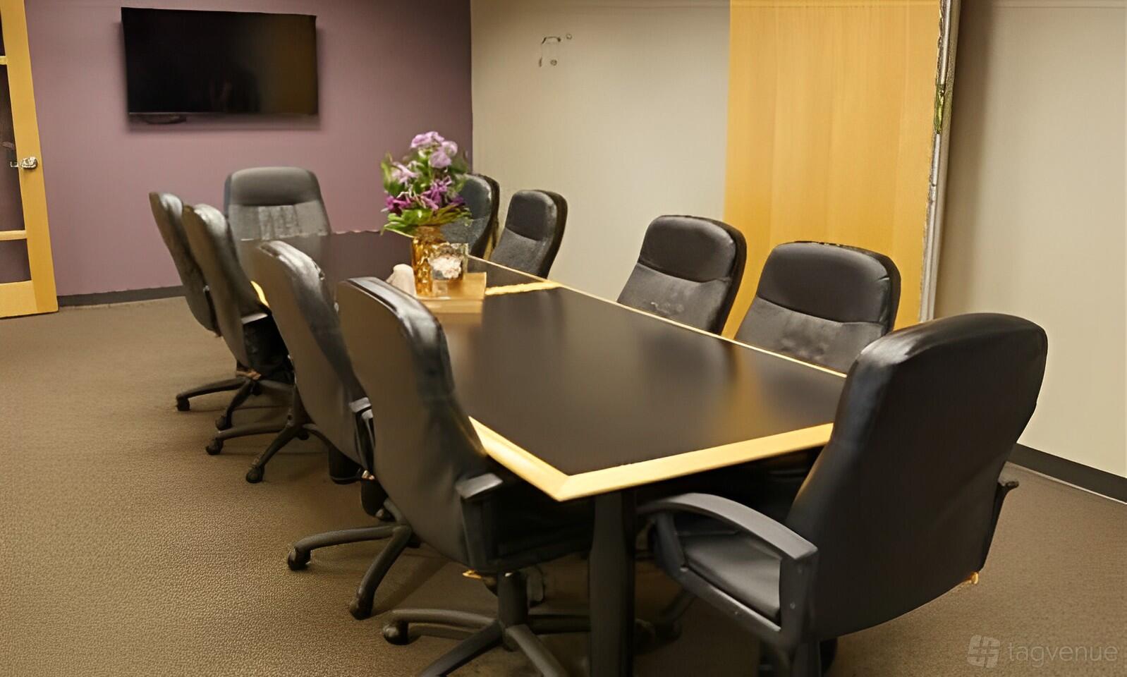 A meeting room with a long conference table, eight black leather chairs, and a wall-mounted TV at Intelligent Office in Rockville, MD.