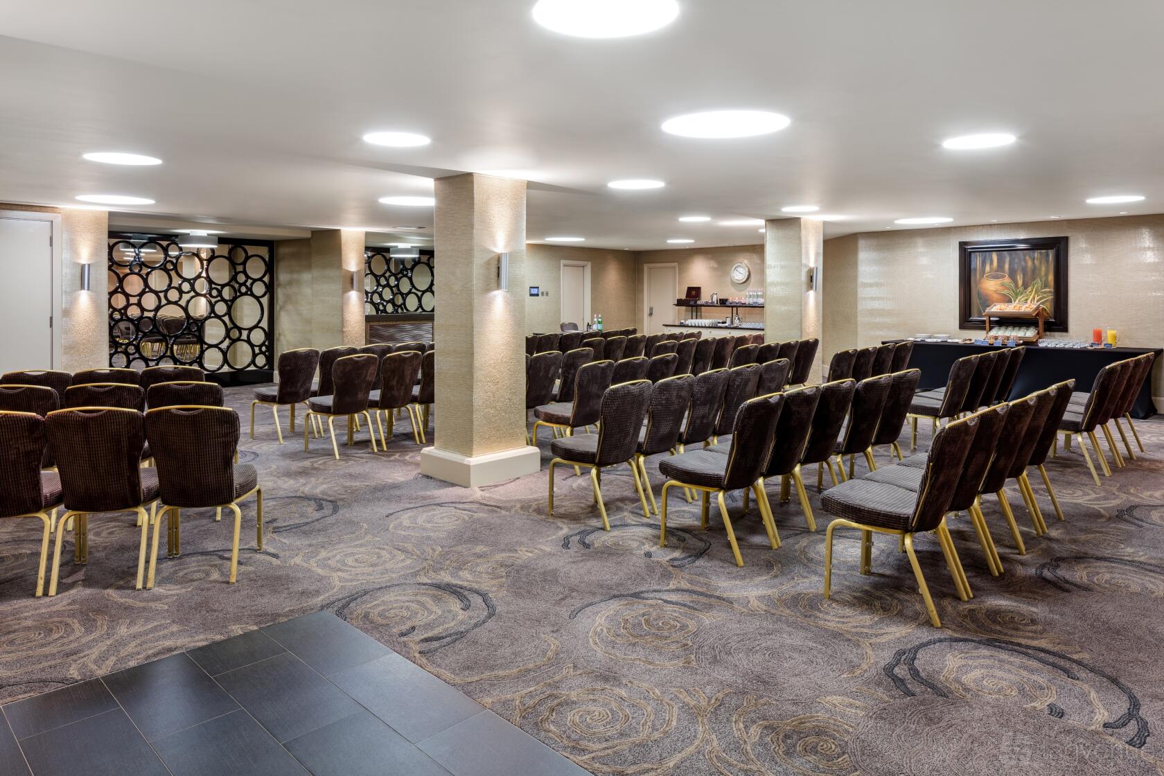 An event space with rows of brown upholstered chairs, round pillar columns, and patterned carpet at Radisson Blu Hotel, London Euston Square.