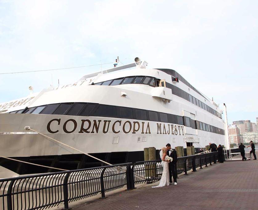 A large white event boat with black lettering docked beside railings at Hoboken NJ Pier