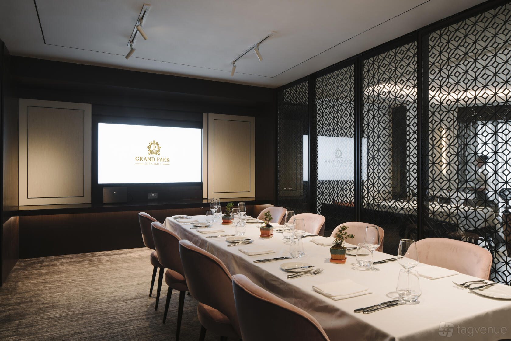 A dining room with a long table set with glassware and blush chairs, partitioned by decorative screens at Grand Park City Hall.