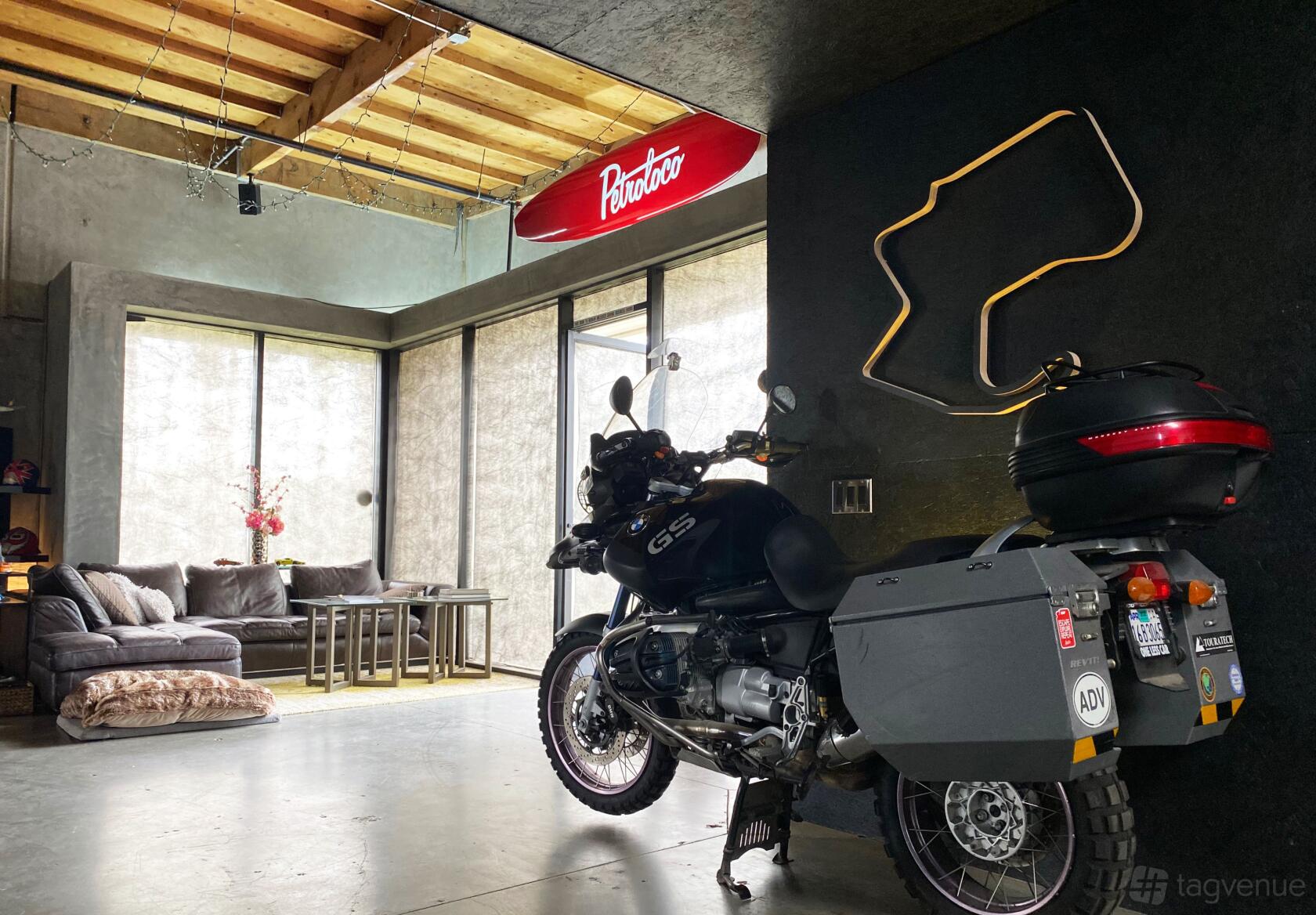 A bar with a motorcycle display, exposed concrete walls, lounge seating, and a neon sign at Petroloco.