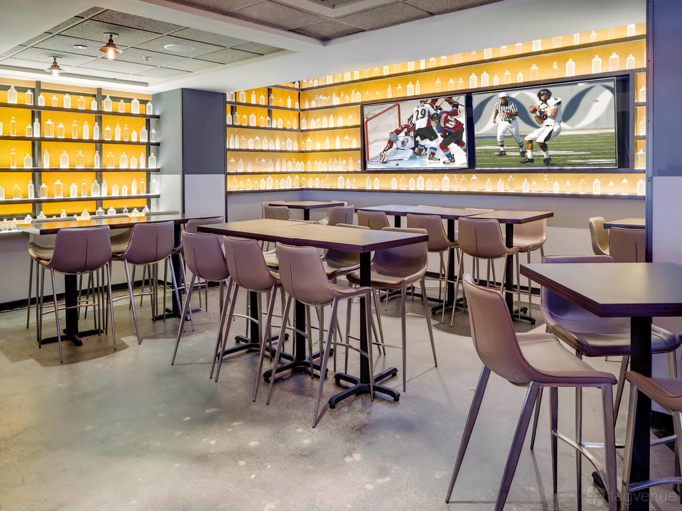 An event space in a bar with backlit bottle displays, high tables, and large TVs at Tom's Watch Bar Los Angeles.