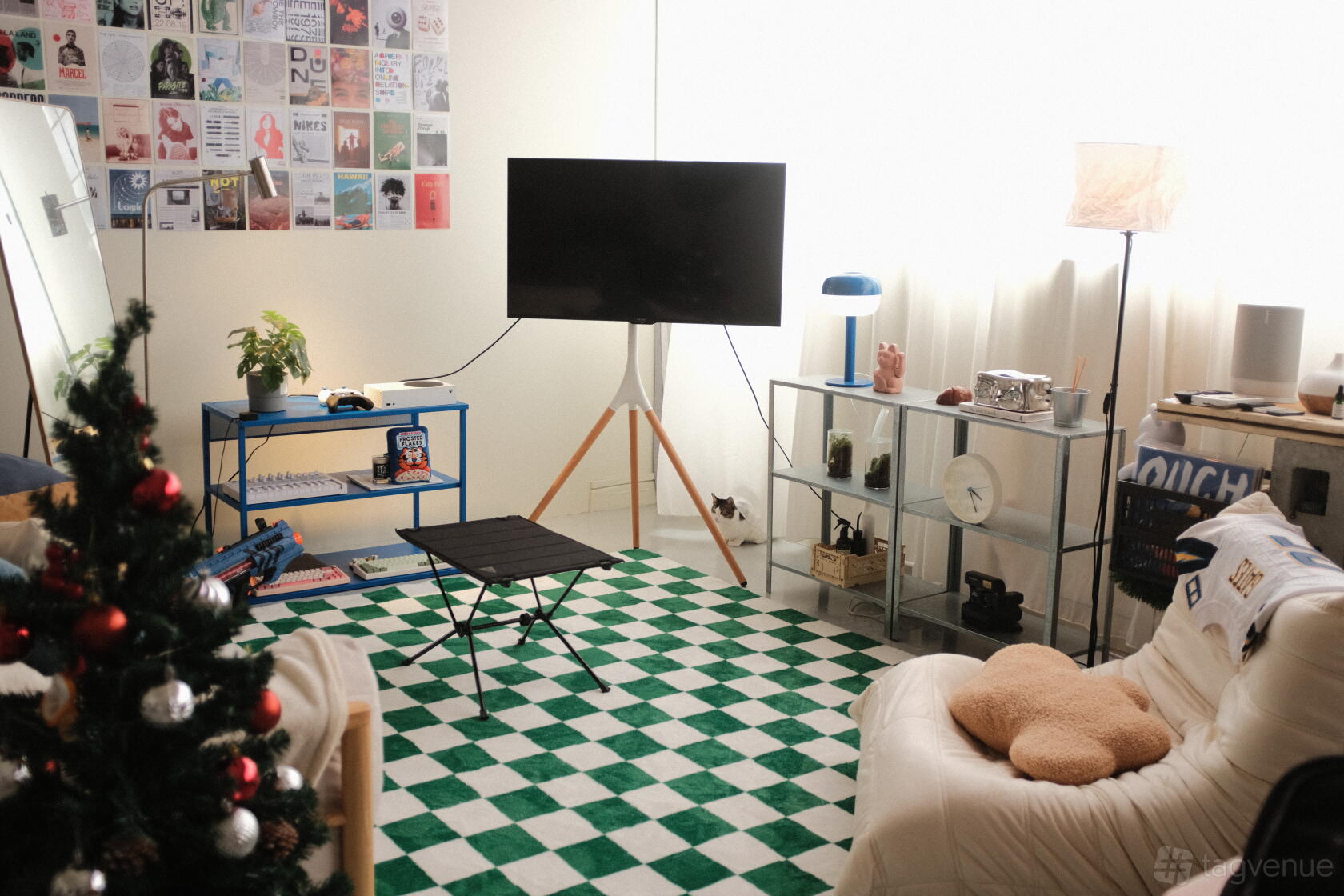 A creative studio with a checkered green and white rug, wall collage, seating, and large TV at Think Beyond Hues | TBH Media.