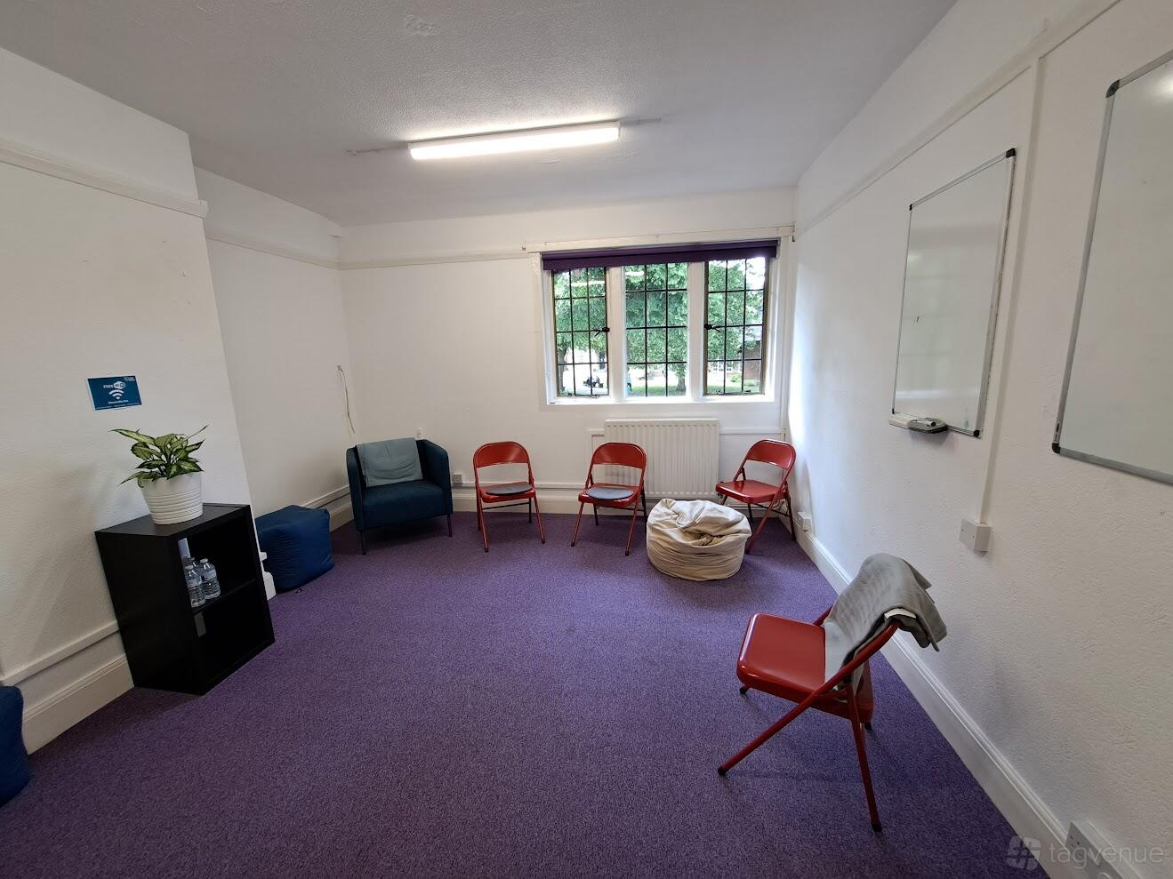 A therapy room with purple carpet, red chairs in a circle, large window, and whiteboards at The Hub on the Green.