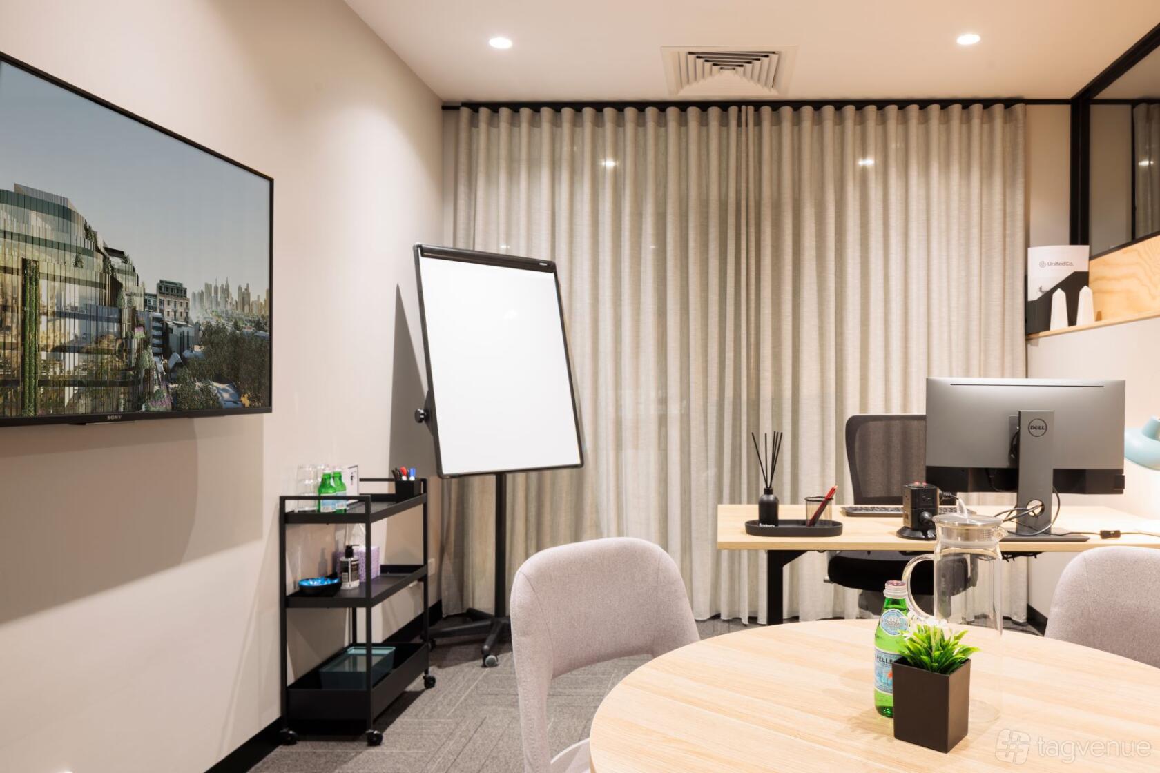 A meeting room with a large monitor, flip chart, round table, and desktop computer at United Co. Fitzroy.