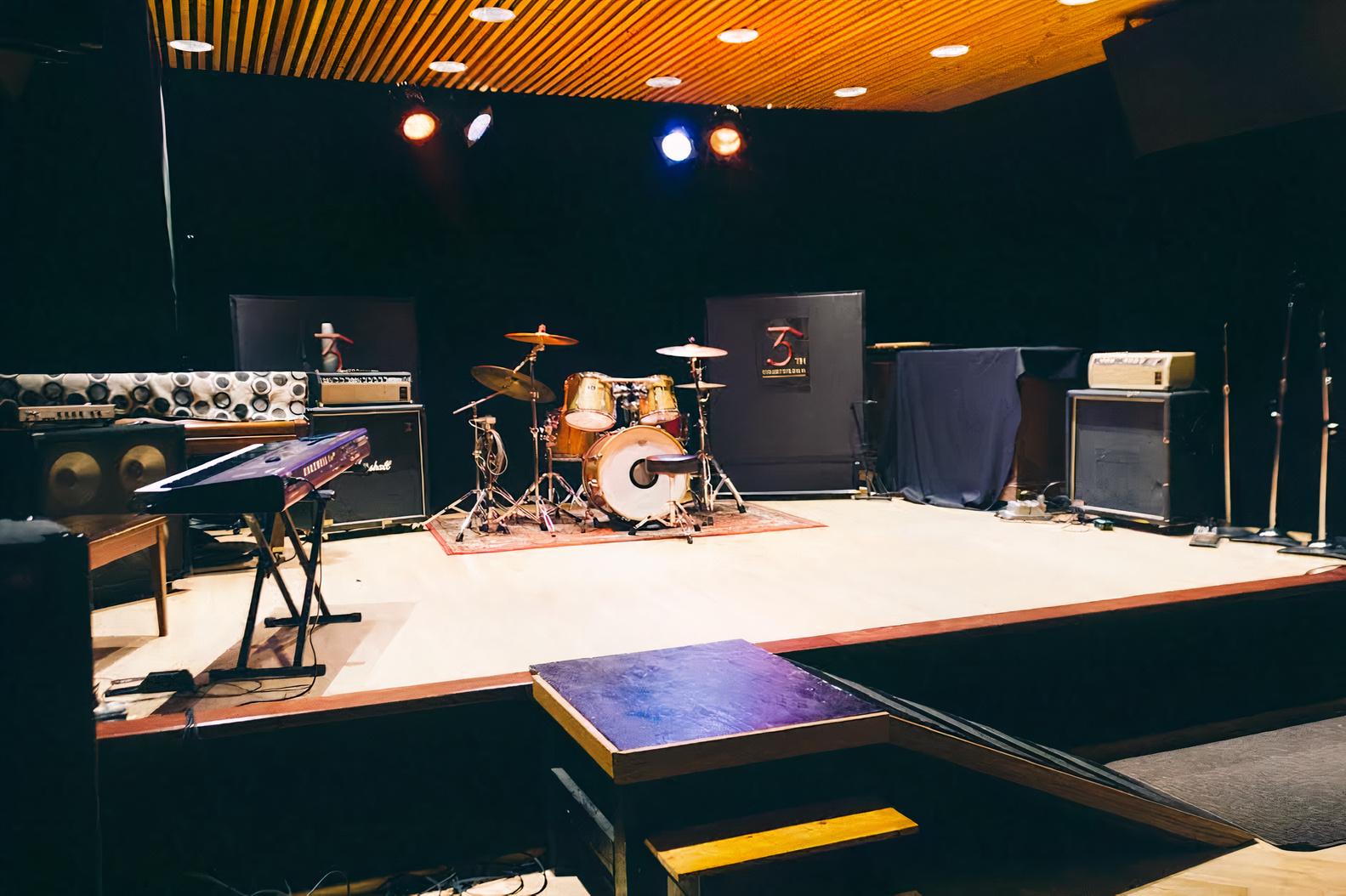 An event venue with a raised stage, drum kit, keyboard, amplifiers, and stage lighting at 35th Street Studios.