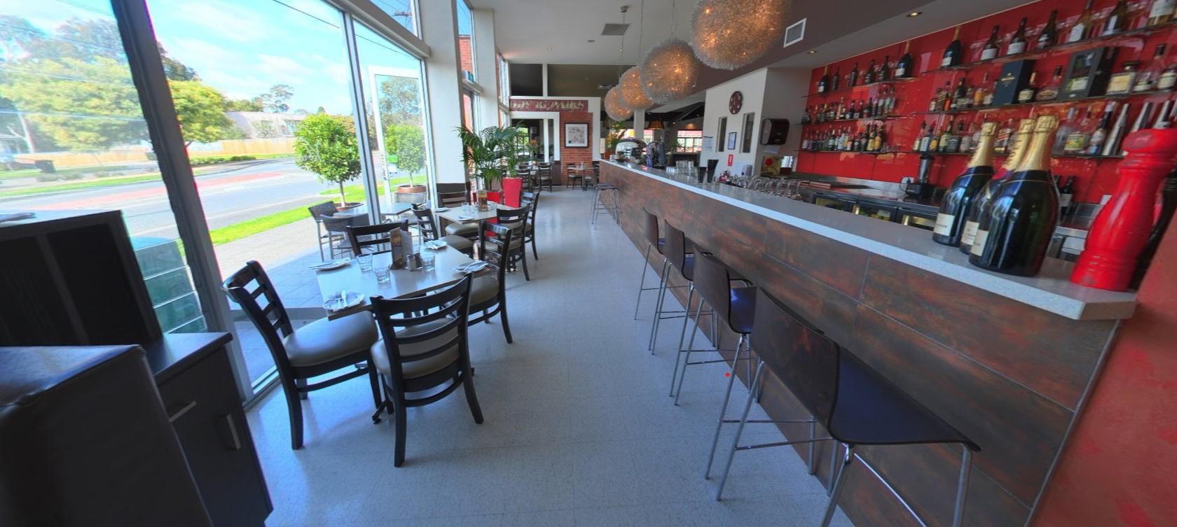 A restaurant bar area with floor-to-ceiling windows, spherical pendant lights, and a long bar at Vibrante Restaurant.