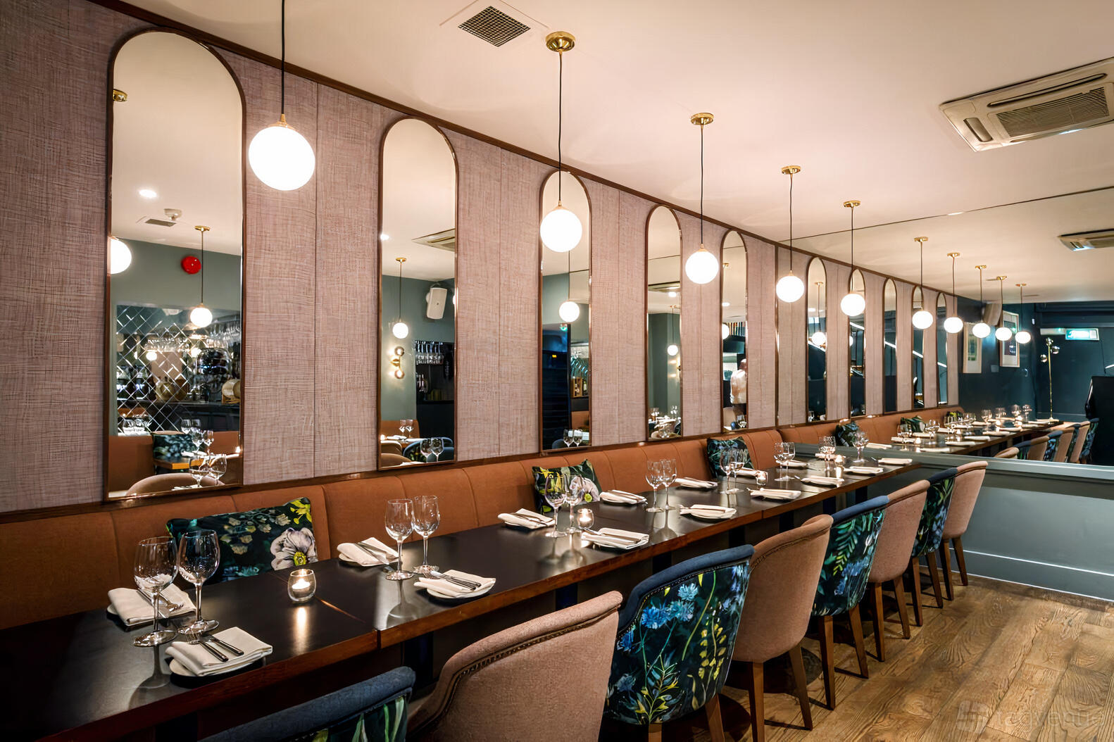 An event space in a restaurant with long tables, modern pendant lighting, and wall mirrors at BANG Restaurant.