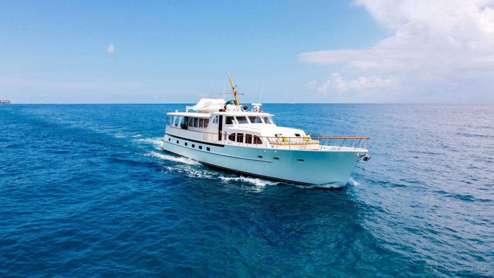 A yacht with a white exterior and open upper deck cruising on clear blue water at Lots Of Yachts/Lots Of Spots South Florida.