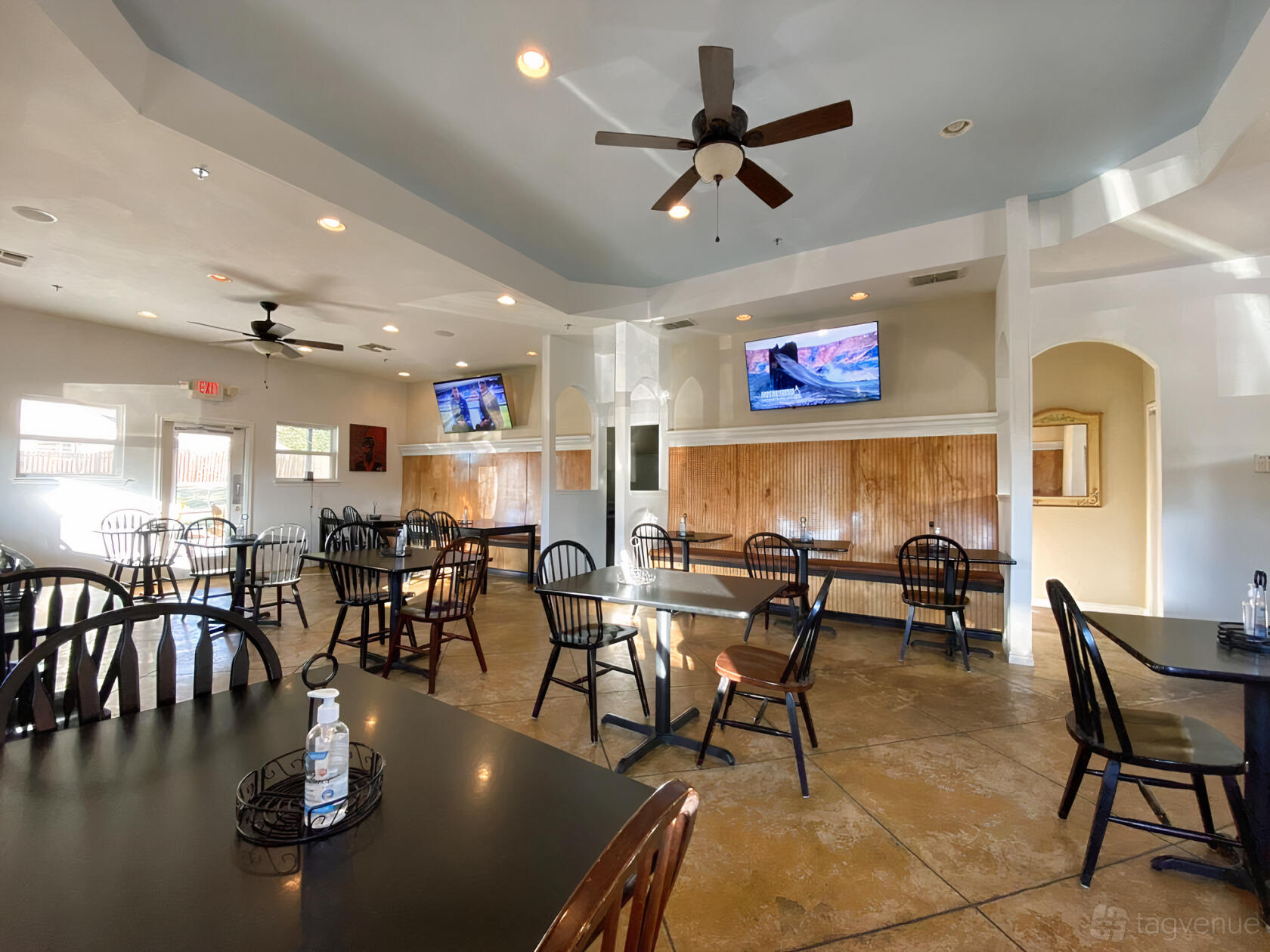 An event space in a restaurant with wooden wall paneling, ceiling fans, and spaced black chairs at Trices Cafe and Lounge.