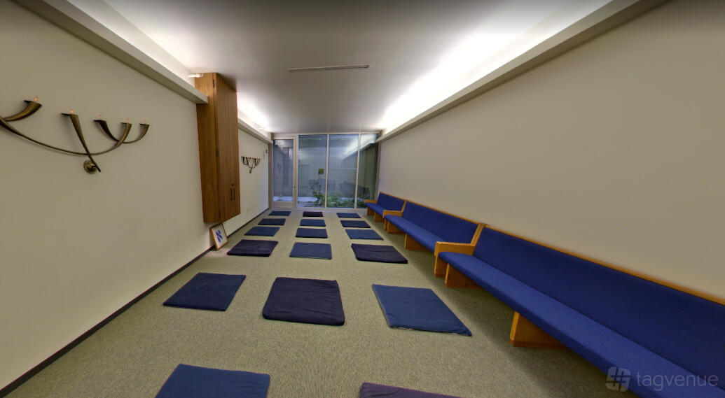 An event venue with blue cushioned bench seating, floor mats, and wall-mounted menorahs at Congregation Beth Sholom.