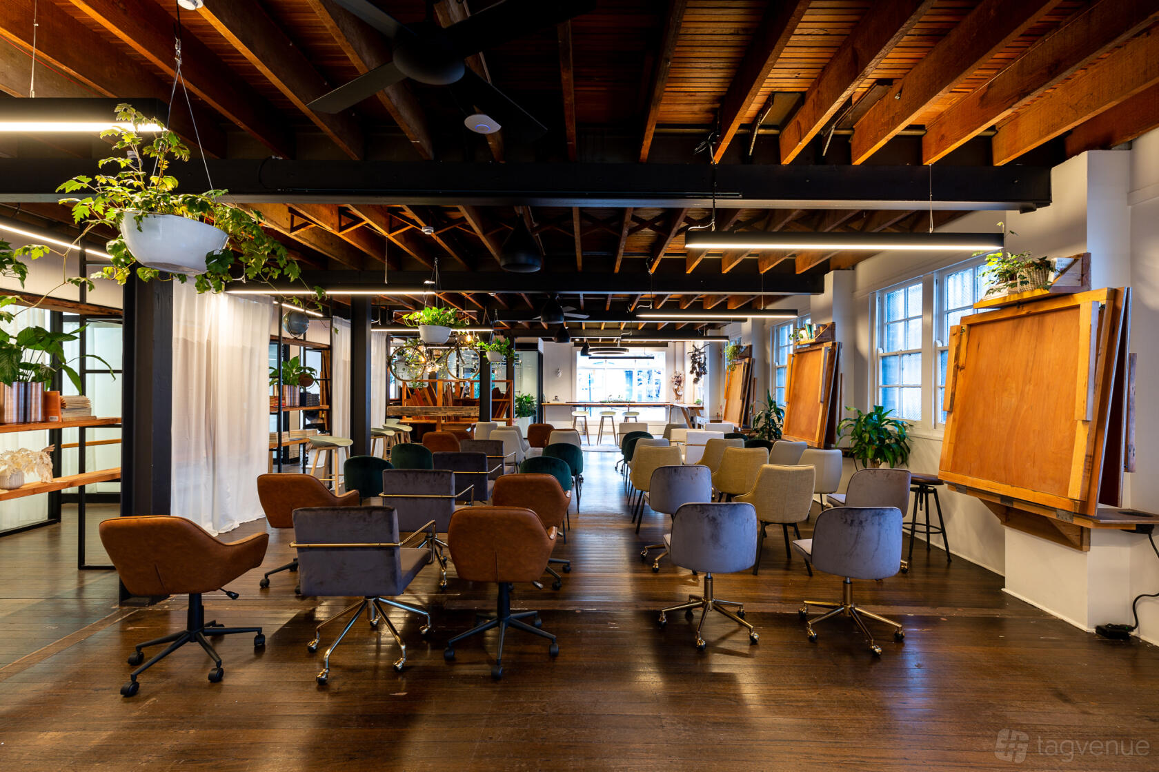 An event space with exposed wooden beams, potted plants, and rows of chairs facing a presentation area at Zeal Spaces.