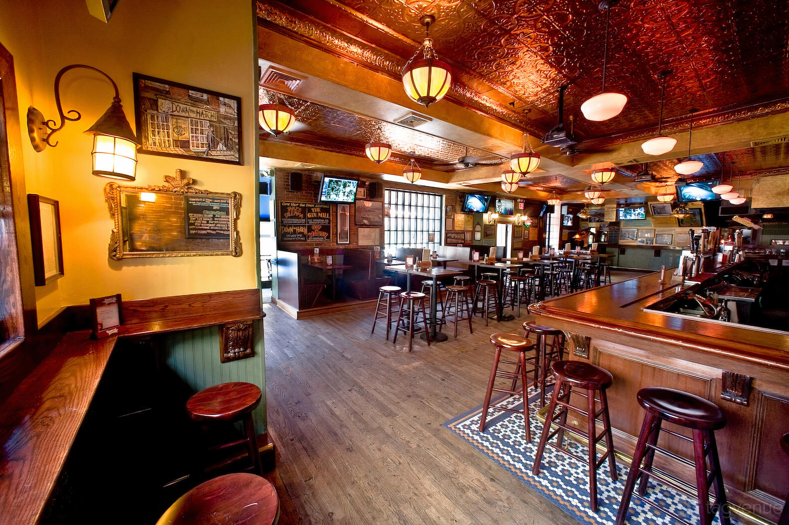 A pub with high-top tables, wooden floors, tin ceiling tiles, and wall-mounted TVs at The East Wing.